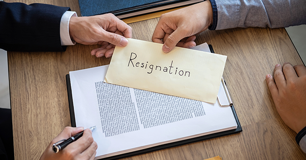Resignation Letter from Employment Law Friend. A man hands his boss an envelope that reads 'resignation', across a wooden desk. Resignation Letter from Employment Law Friend. A man hands his boss an envelope that reads 'resignation', across a wooden desk.
